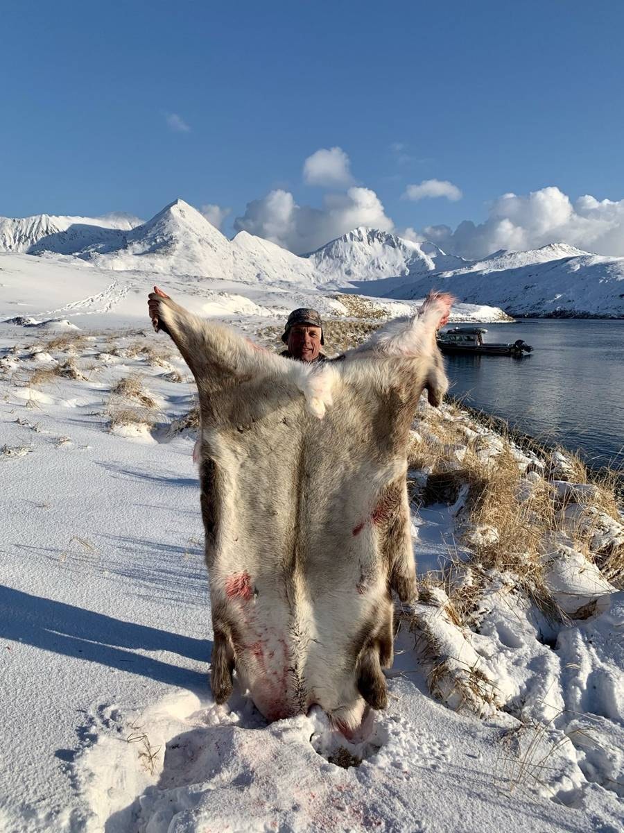 Hunter with Caribou hide, snowy Adak peaks behind
