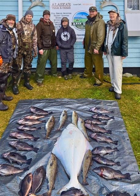 Group at Alaska sign with full fish haul