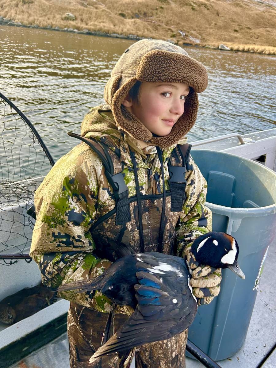 Young hunter in camo holding a Harlequin duck on the boat
