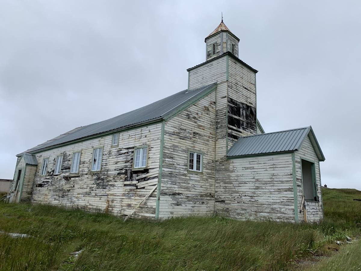 Weathered white chapel with steeple on Adak Island, tundra hills behind