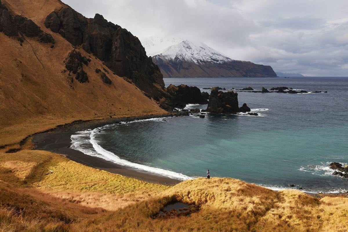 Rocky Adak coastline with snow-capped peak and teal water