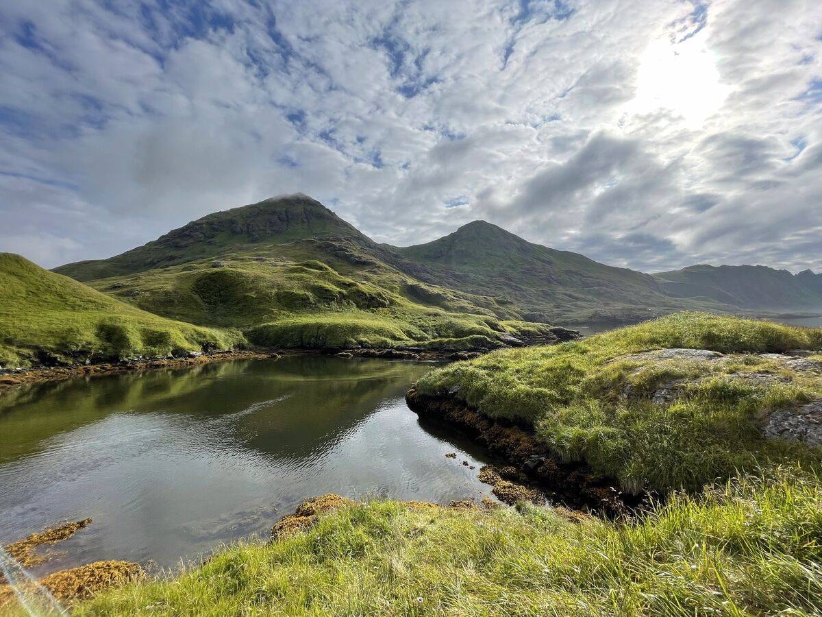 Lush green Adak tundra with a mountain tarn, twin peaks, and dramatic sky