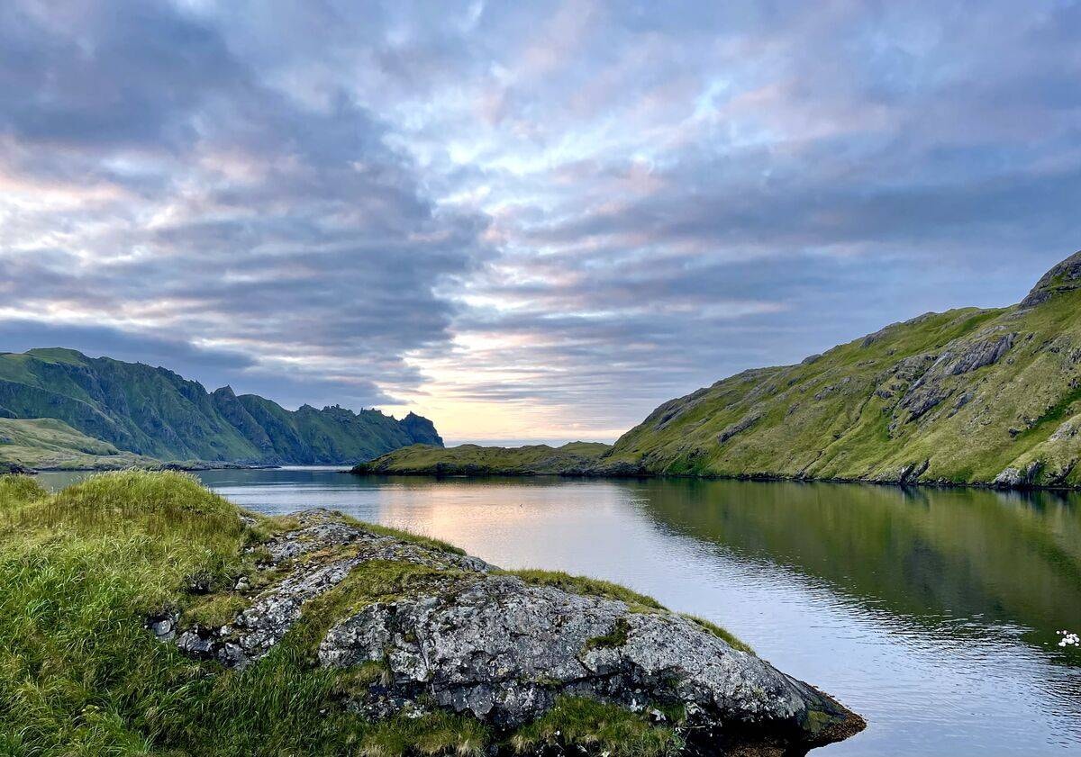 Adak lake at dusk, green tundra hills and dramatic sky reflected in the water