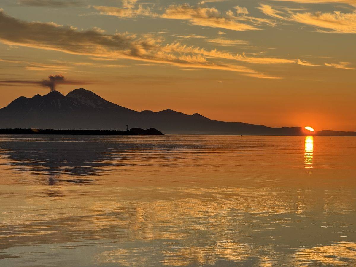 Volcano silhouette at sunset over calm Adak waters