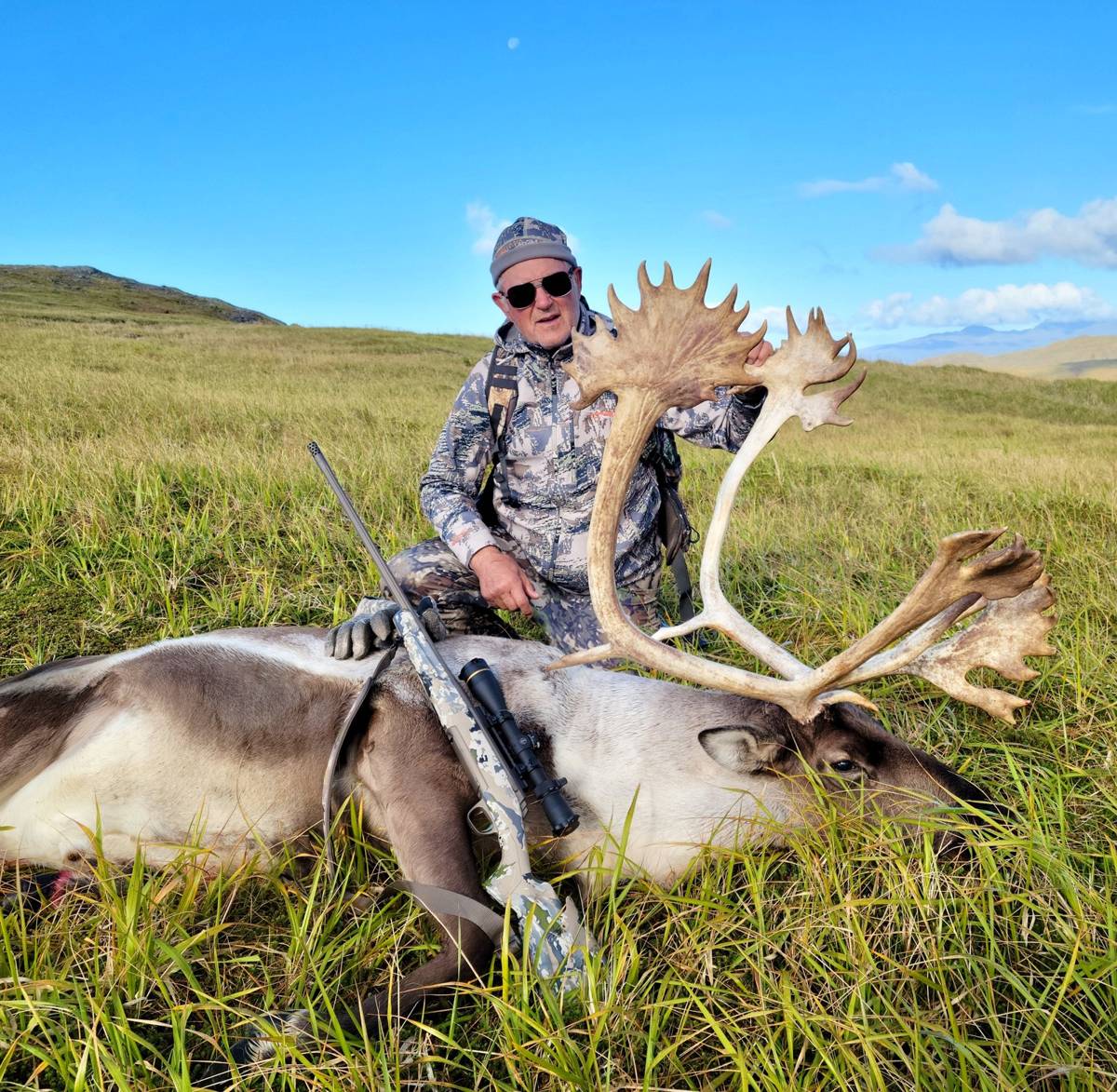 Hunter with scoped rifle and trophy Caribou on a sunny day