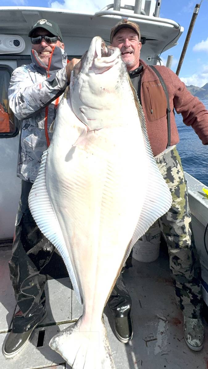 Two guests on the boat hoisting a giant Halibut by the gills